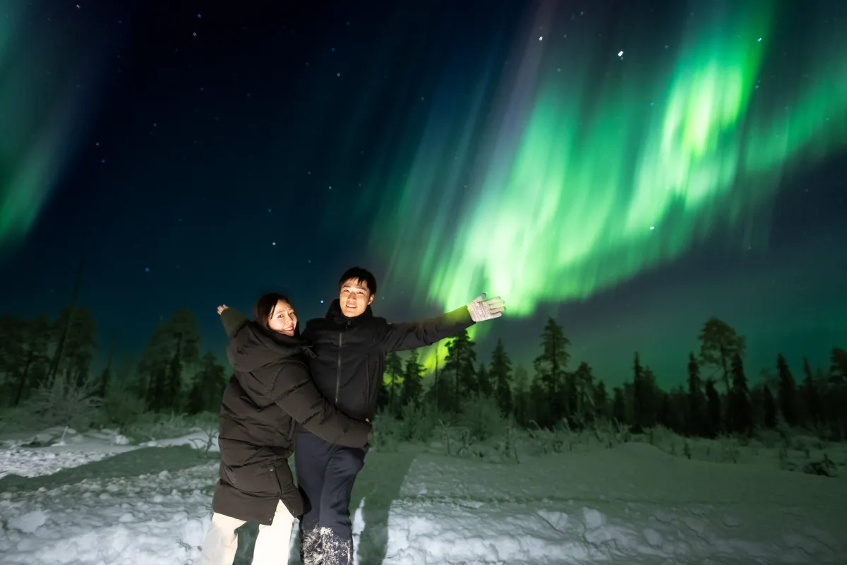 Guests with arms raised under green and violet aurora
