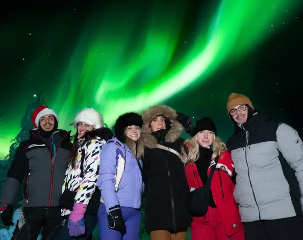 在罗瓦涅米附近的 Experience Tours 追光之旅中,七位客人在明亮的绿色极光下微笑